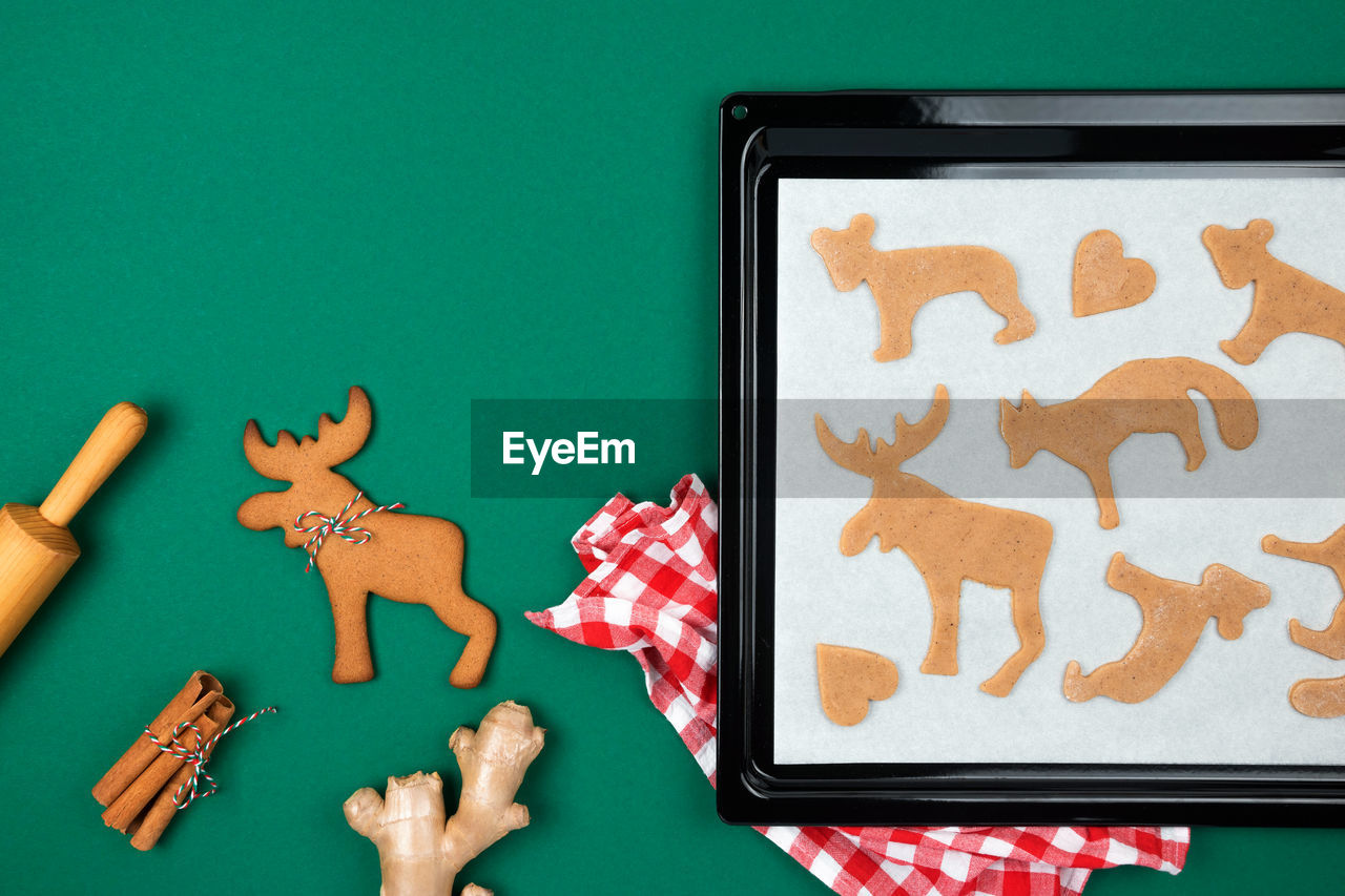 Top view of christmas gingerbread cookies from raw dough on baking tray, fresh ginger, cinnamon