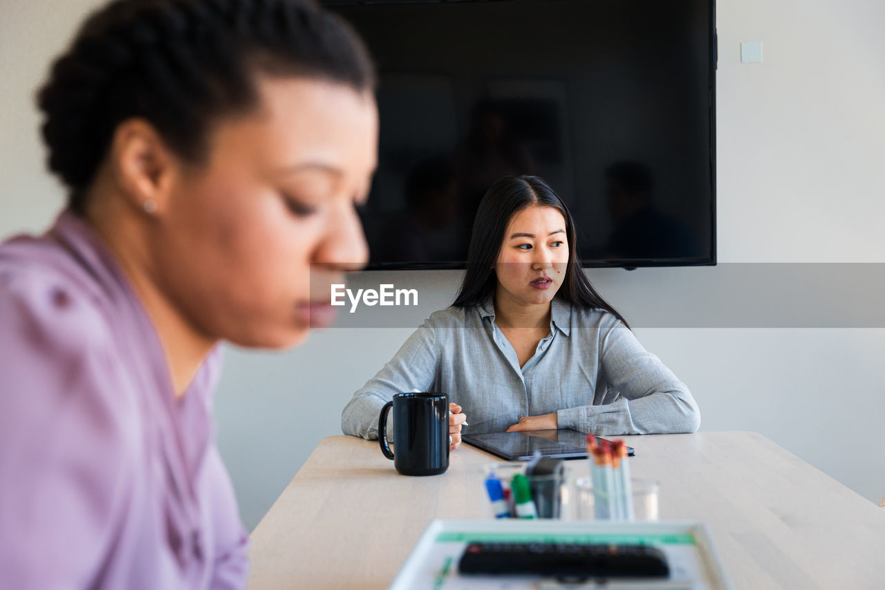 Thoughtful businesswoman using graphics tablet while sitting with colleague in office