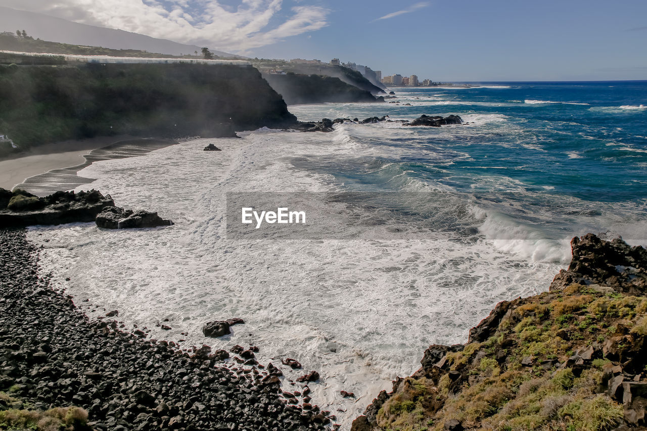 Panorama of a rocky ocean coastline with a city view behind, tenerife
