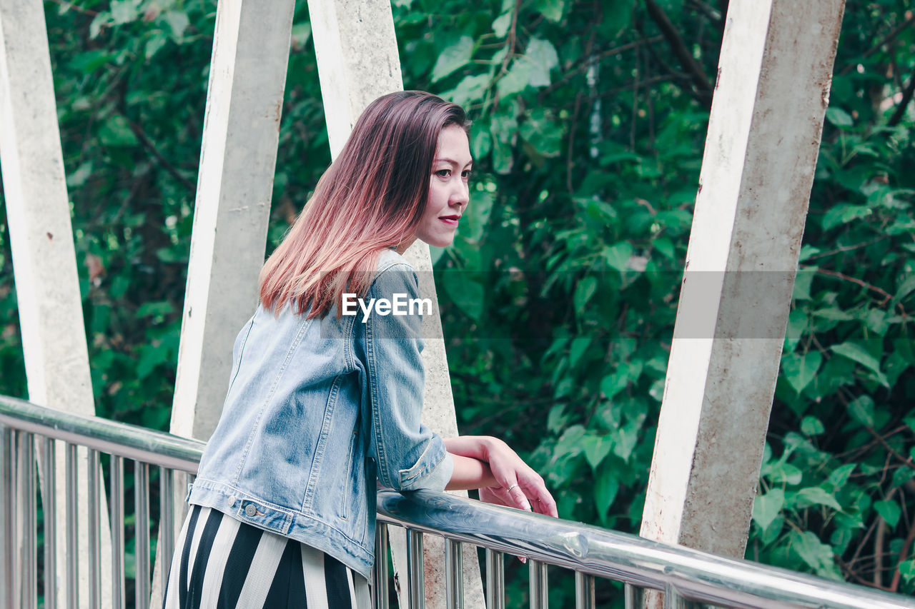 WOMAN LOOKING AWAY WHILE STANDING ON RAILING