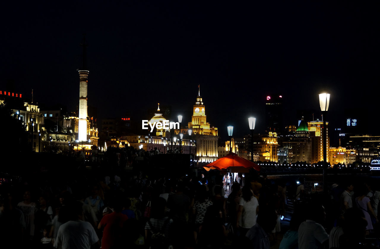 CROWD AT ILLUMINATED CITY AGAINST SKY