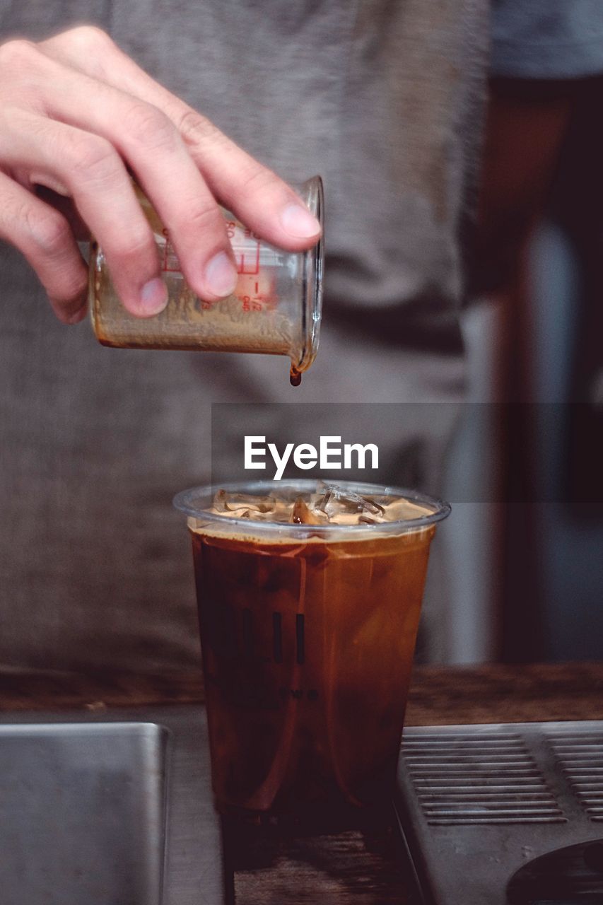 Midsection of person pouring iced coffee in glass