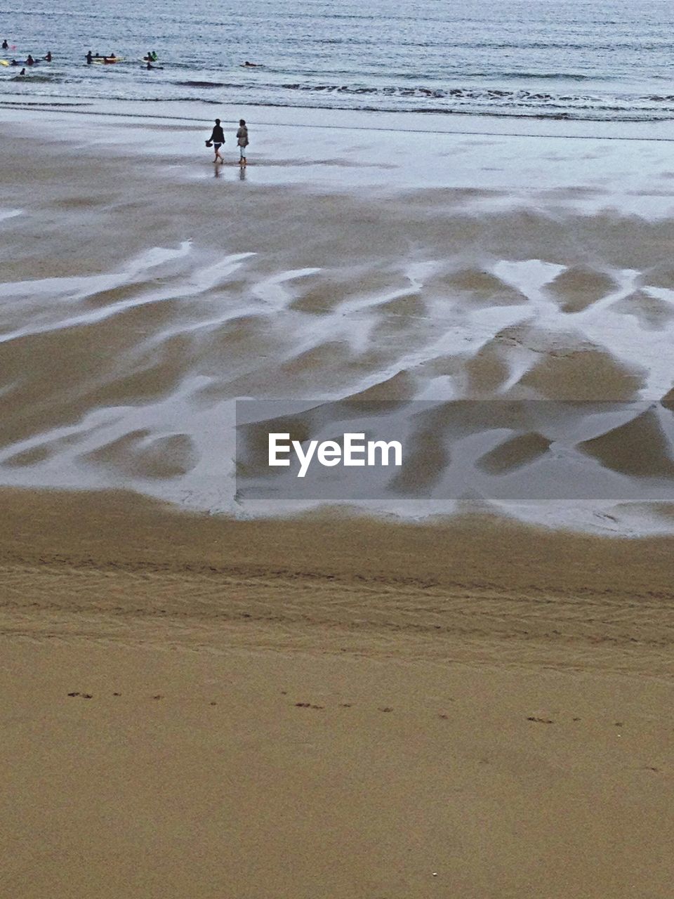 Two silhouette people walking on calm beach