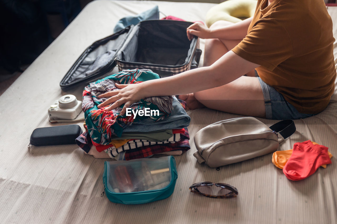 Woman folds clothes from a pile of selected items such as sunglasses, polaroid camera, cosmetic bag