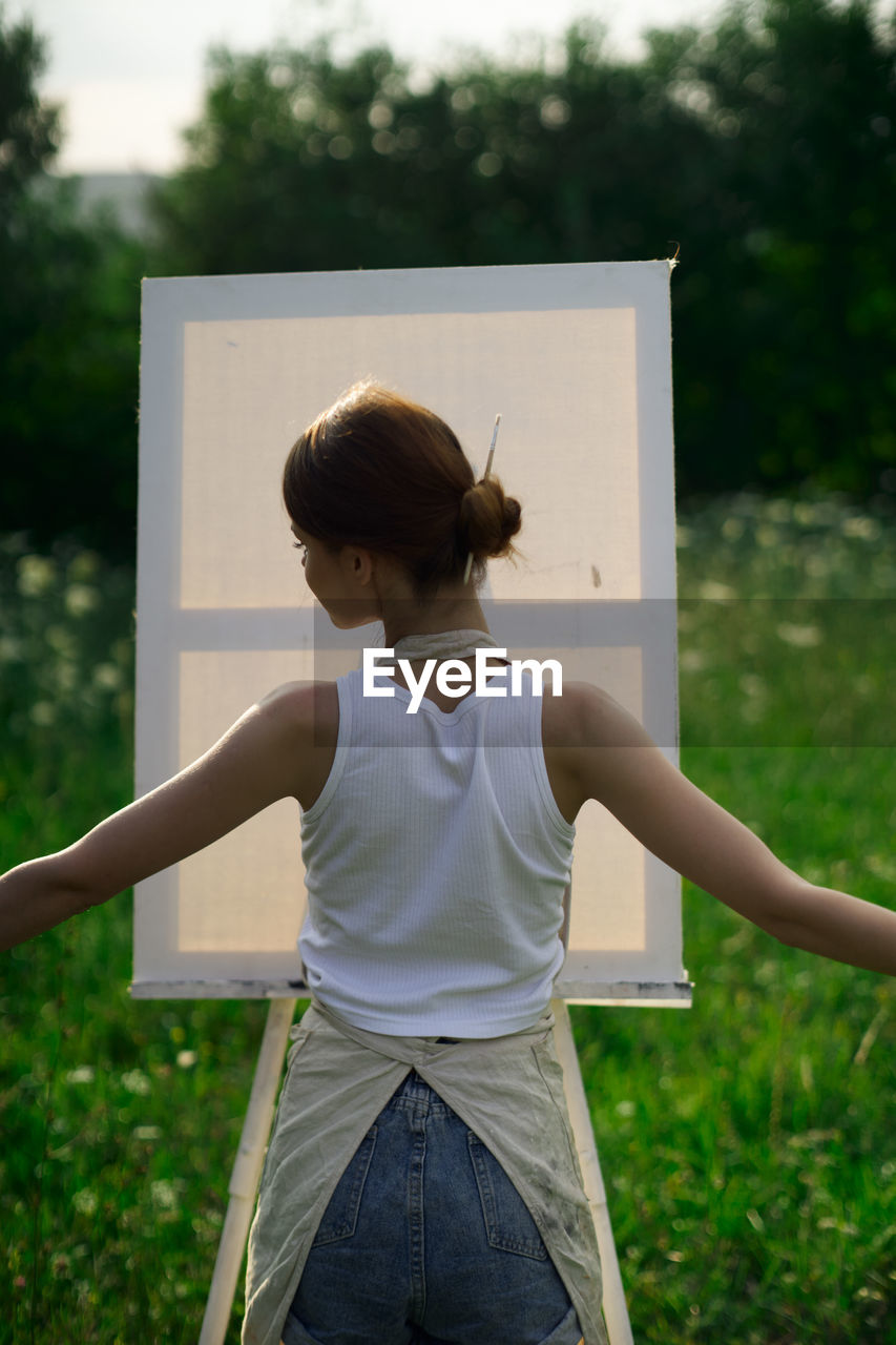 REAR VIEW OF WOMAN STANDING ON FIELD AGAINST TREES