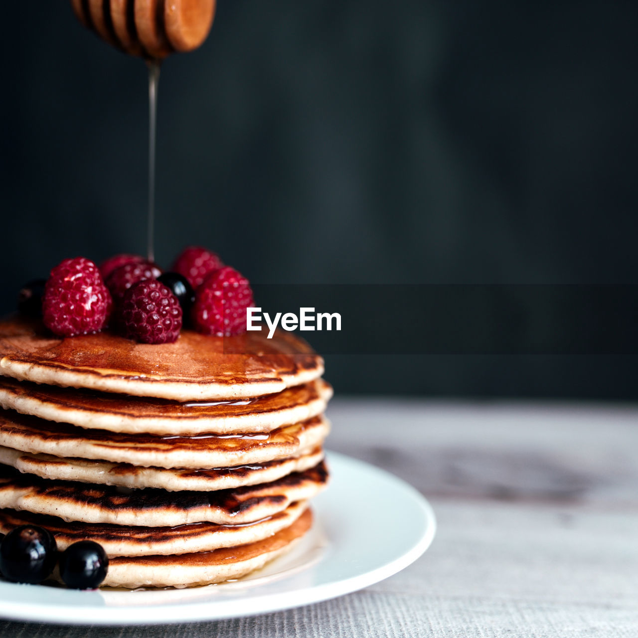 Juicy pancakes with berries and honey on a white plate, spoon, wooden table. high quality photo