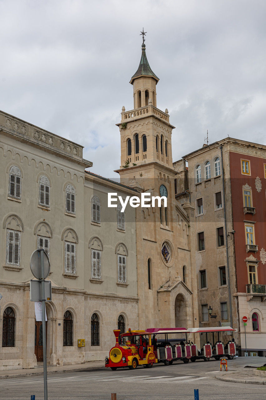 A historic european street scene featuring a beige stone church with a tall clock tower.