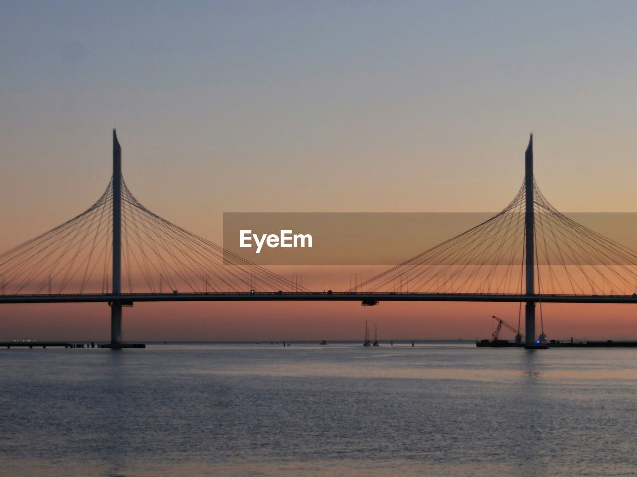 Suspension bridge over sea against sky during sunset