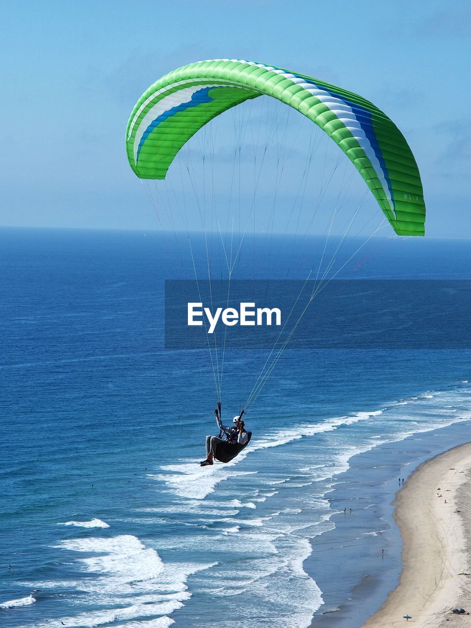 Person paragliding over sea against sky