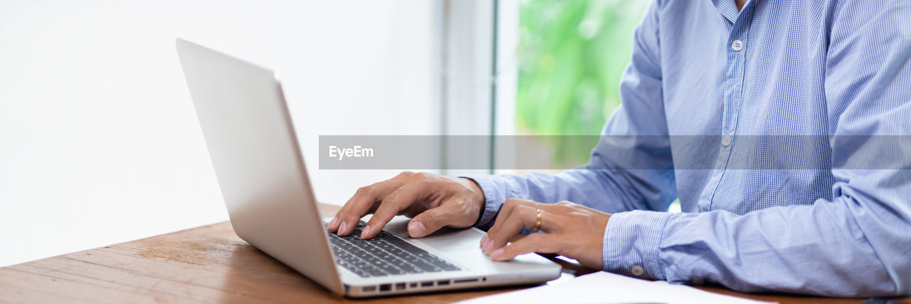 REAR VIEW OF MAN USING LAPTOP