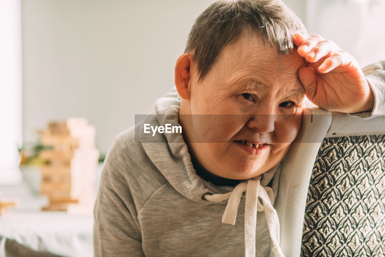 Portrait of an elderly smiling woman with down syndrome in a sunny room