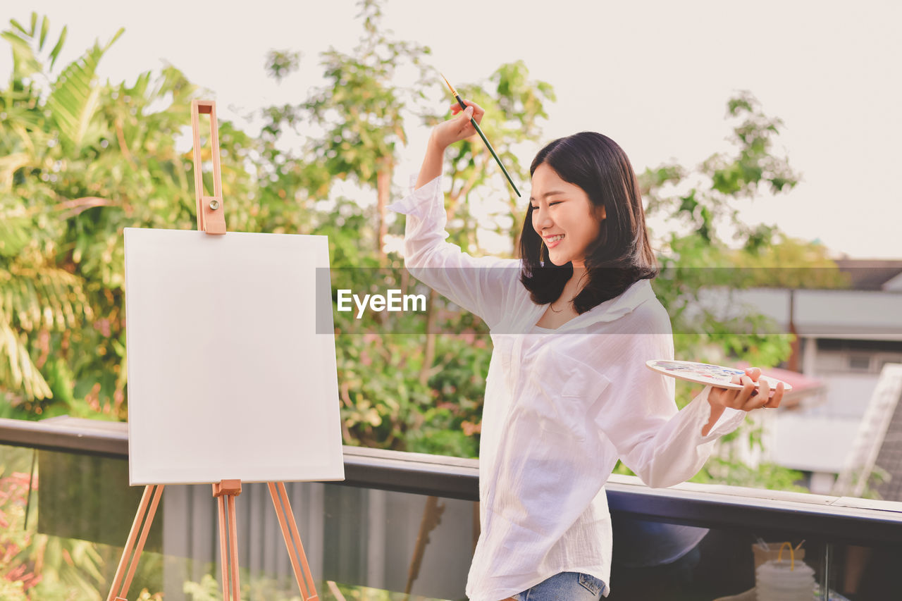 Smiling woman standing by canvas against sky