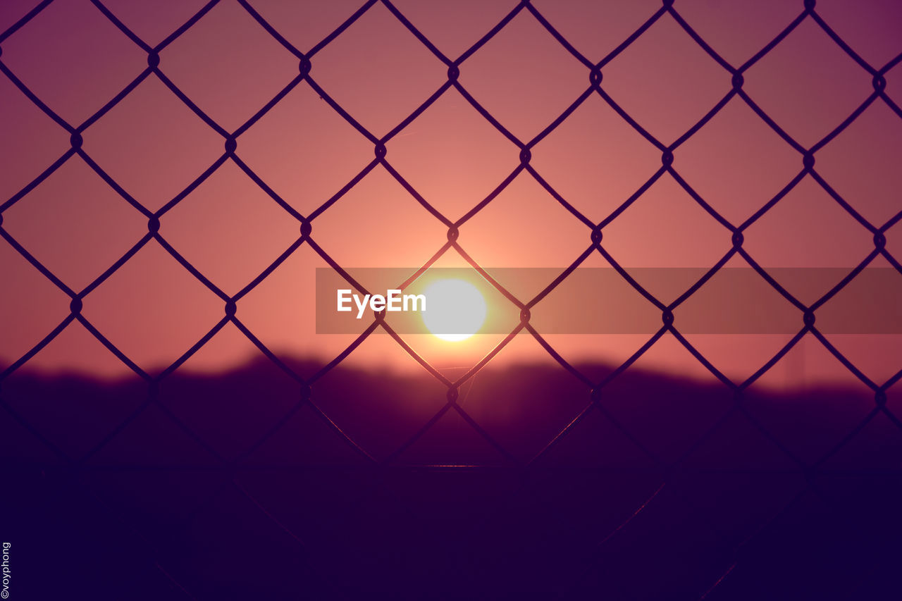 Close-up of silhouette chainlink fence against sky during sunset