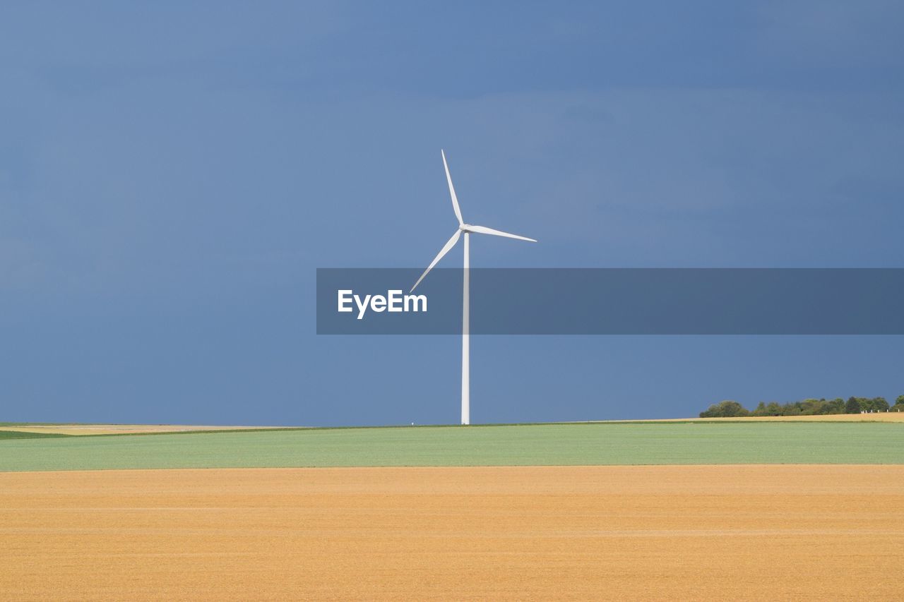 Wind turbines on field against blue sky