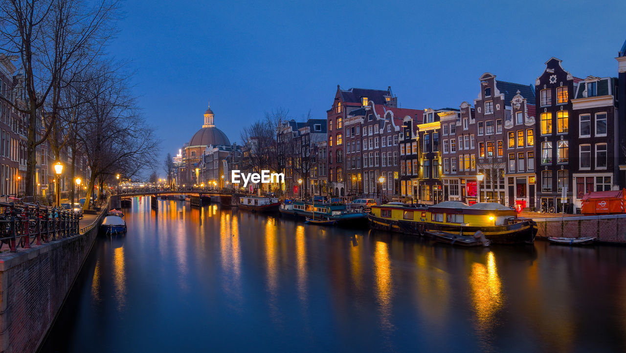 Singel canal amidst illuminated buildings against sky at dusk