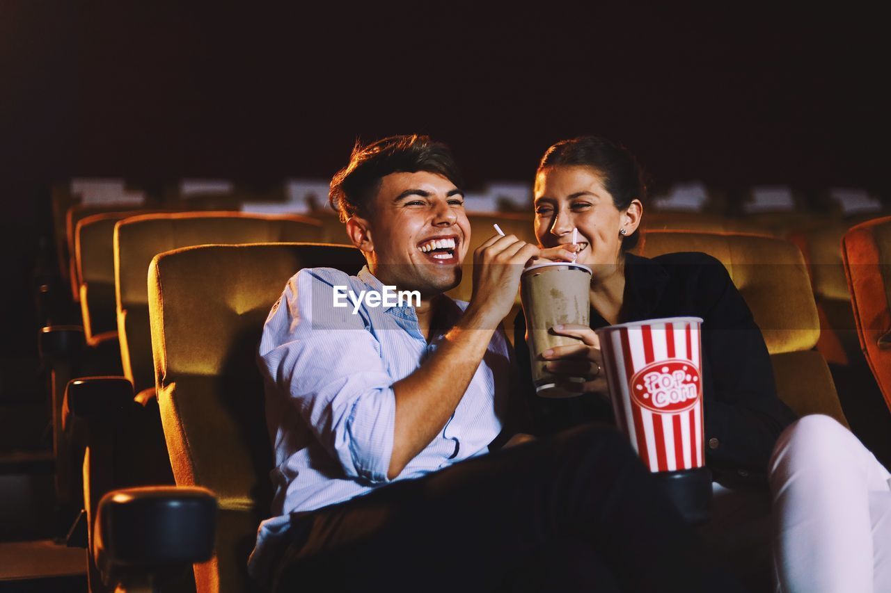 Happy couple having drink while sitting in movie theater