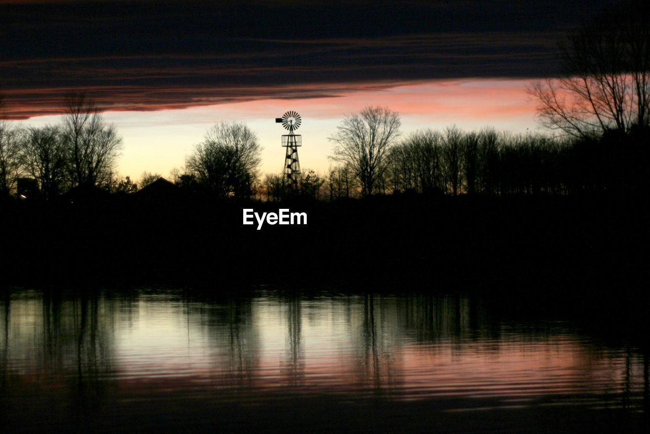 Silhouette trees by lake against sky during sunset