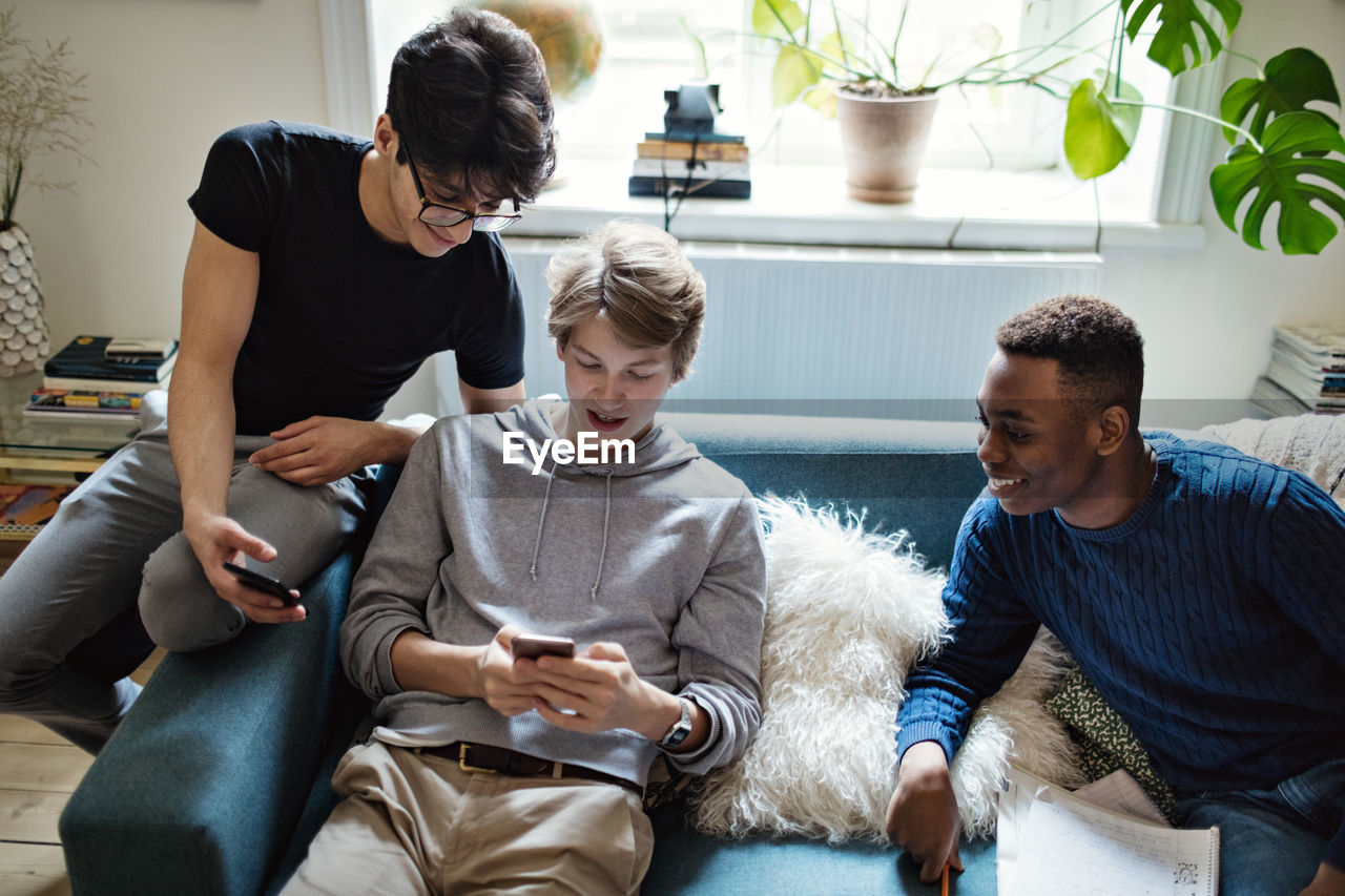 High angle view of social media addicted friends using smart phones on sofa during homework in living room