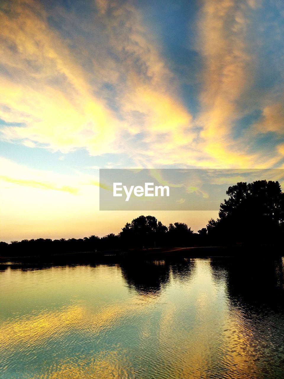 REFLECTION OF SILHOUETTE TREES IN LAKE AGAINST SKY DURING SUNSET