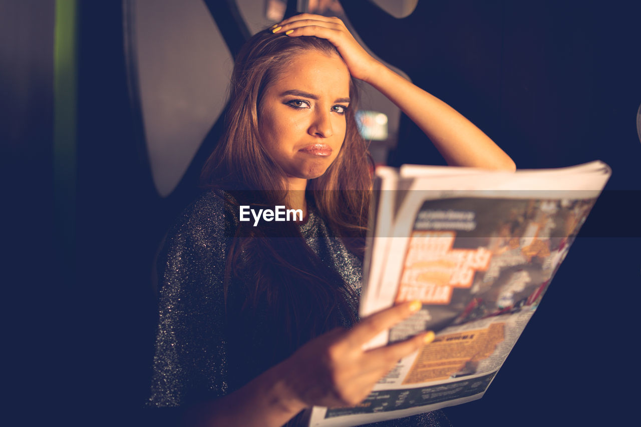 Portrait of sad young woman with magazine at home