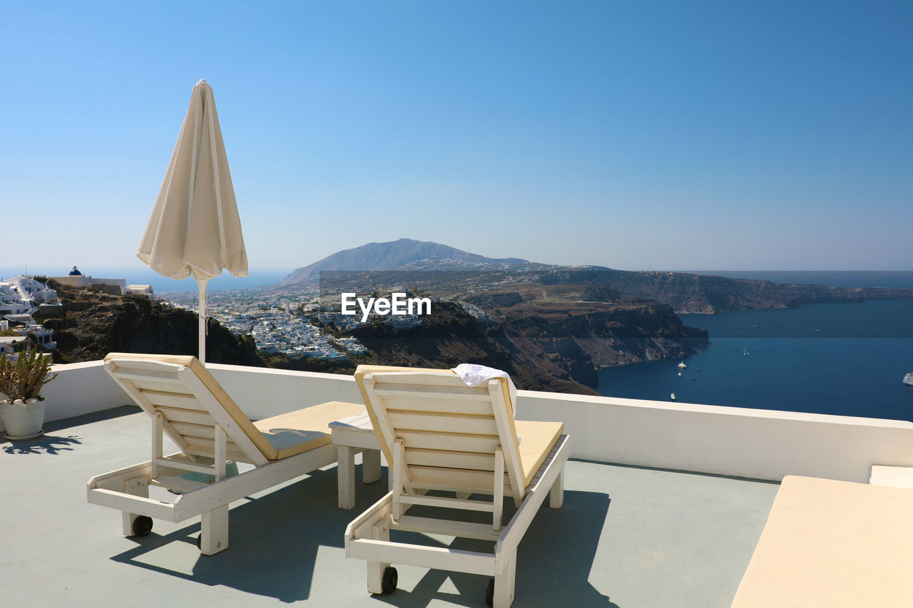 Chairs and tables by sea against clear blue sky