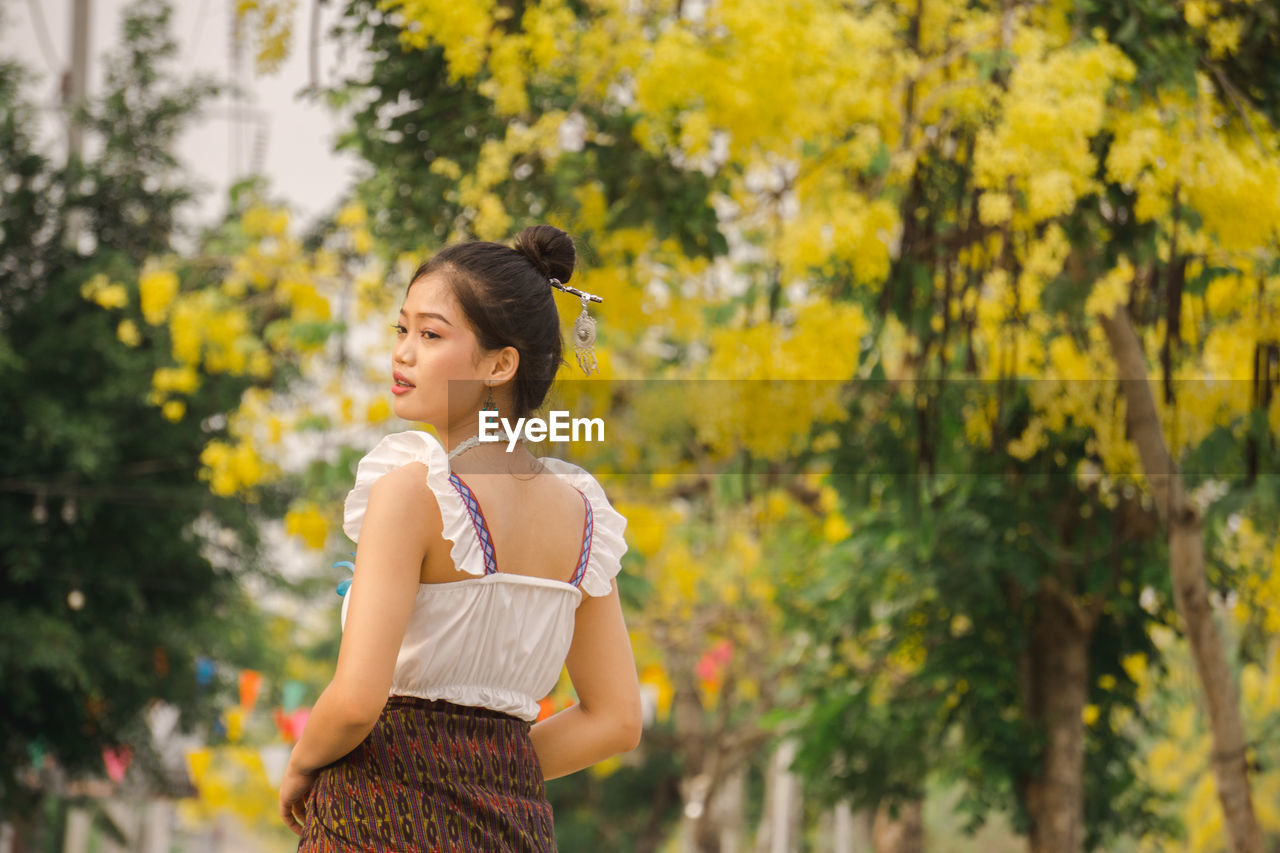 FULL LENGTH OF WOMAN STANDING BY YELLOW PLANTS