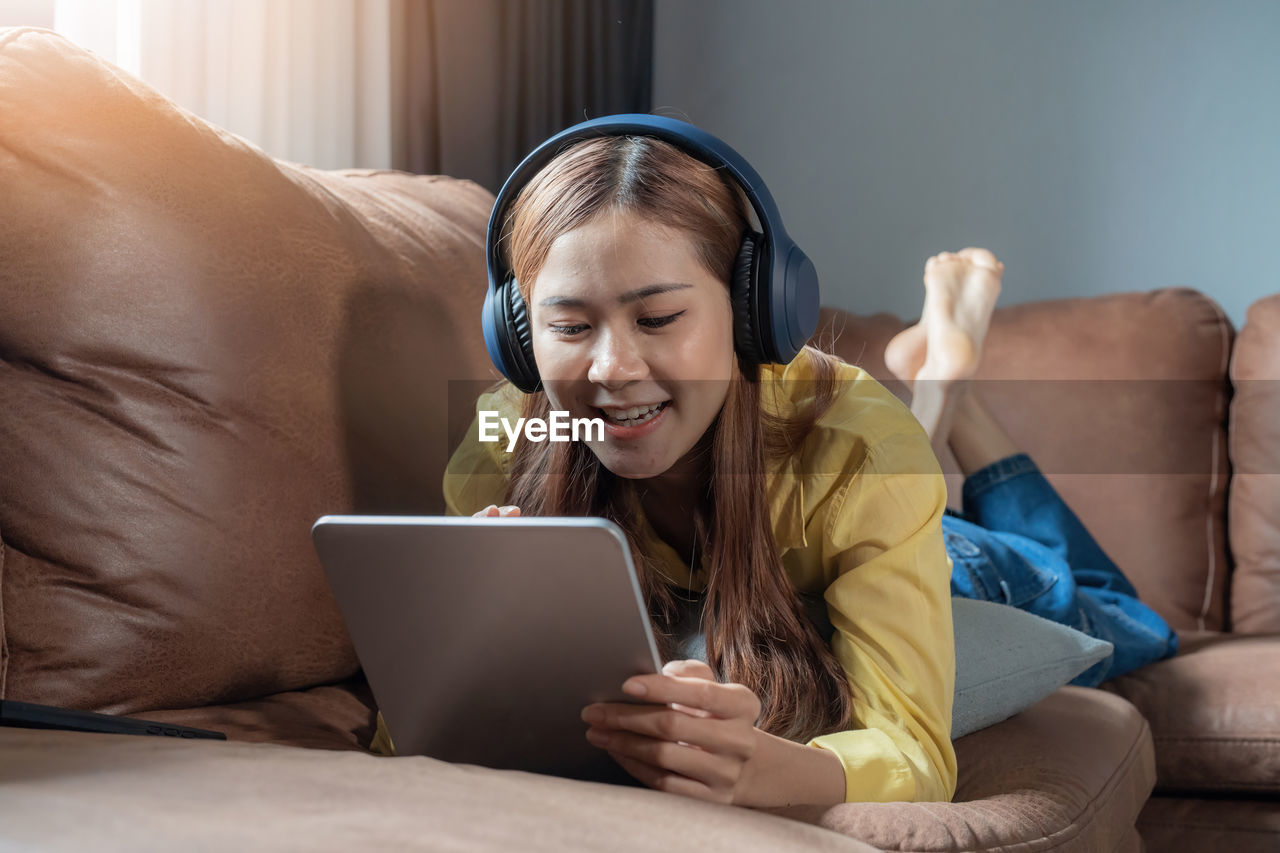 portrait of young woman using laptop while sitting on sofa at home