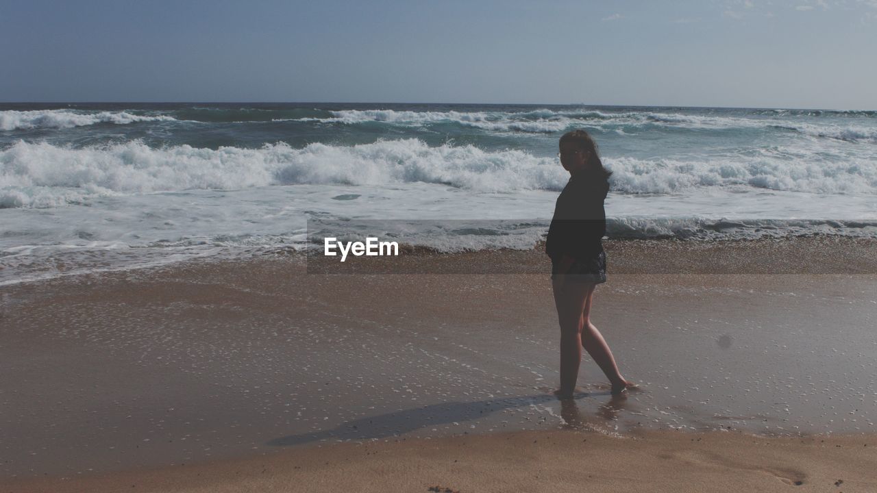 REAR VIEW OF WOMAN STANDING AT BEACH