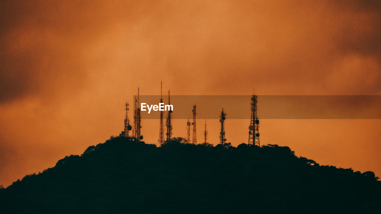 Low angle view of silhouette communications tower against sky during sunset