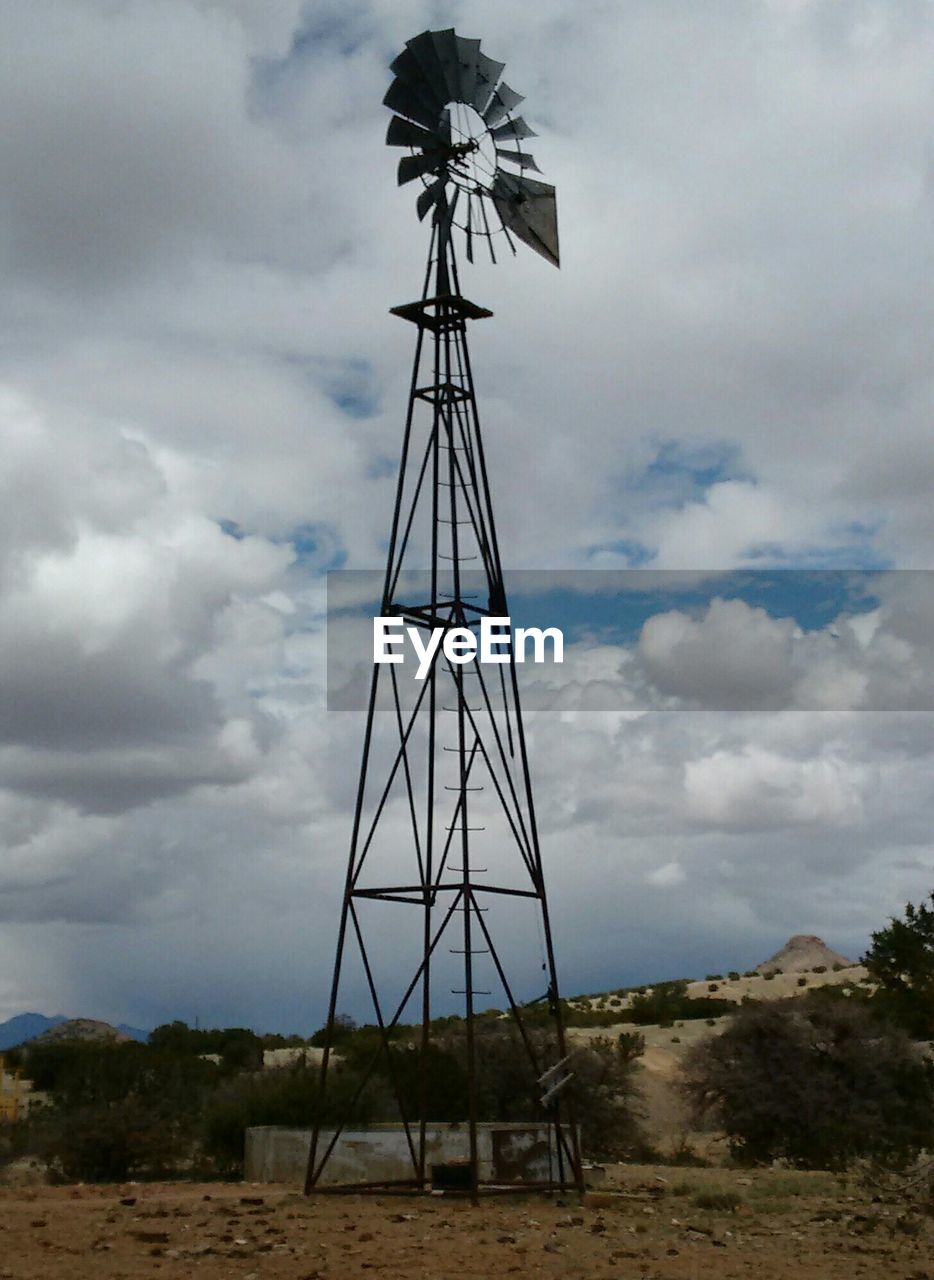 WINDMILLS ON LANDSCAPE AGAINST CLOUDY SKY