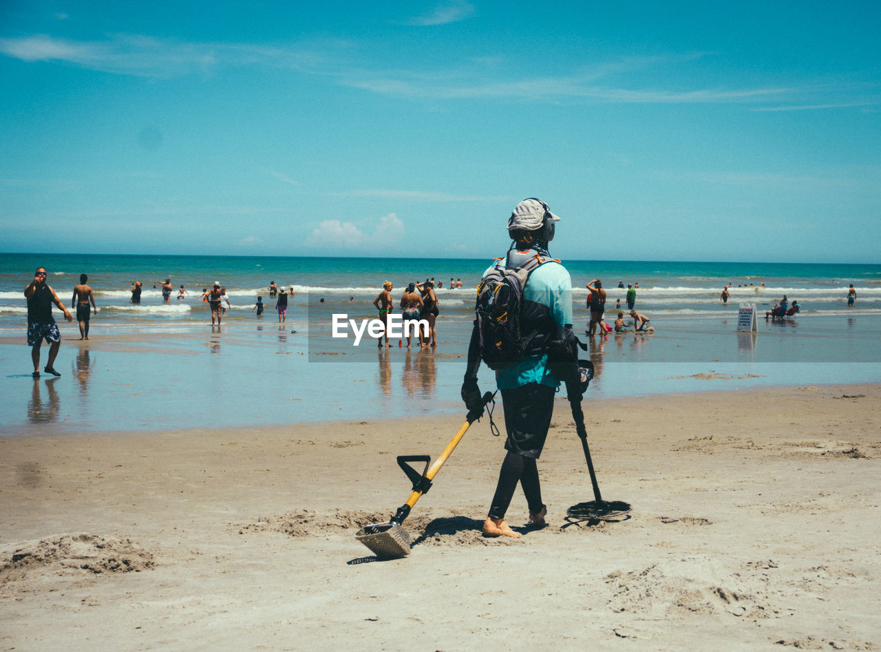 Person with equipment walking at beach against blue sky