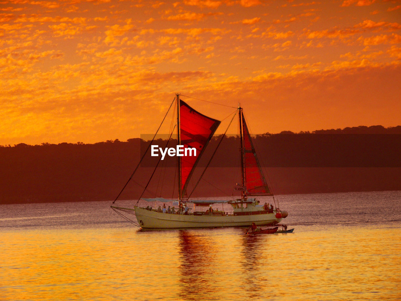 SAILBOATS SAILING ON SEA AGAINST ORANGE SKY