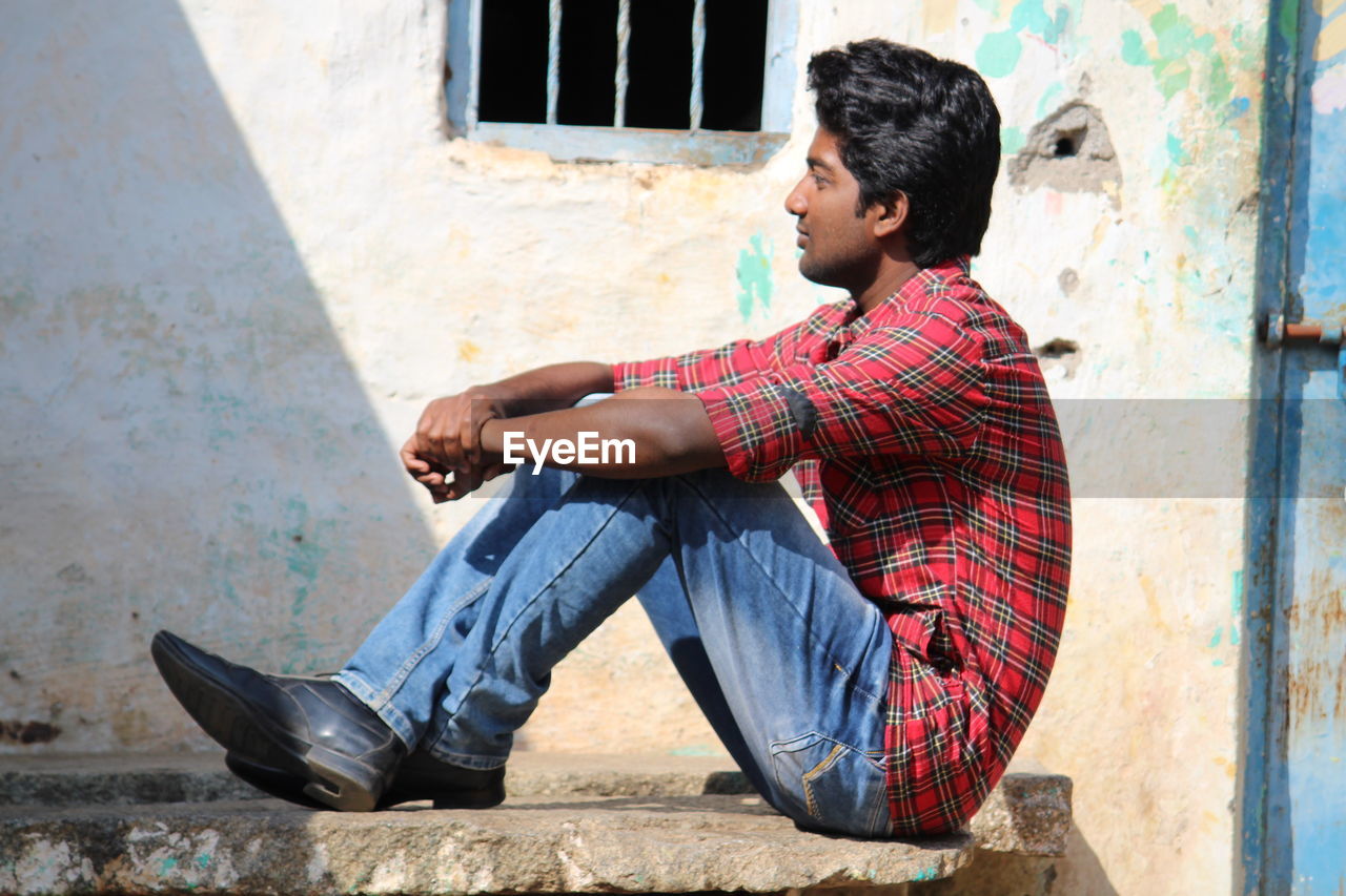 SIDE VIEW OF MAN SITTING AGAINST WALL