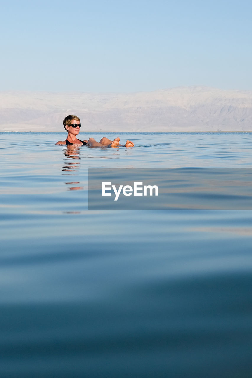 Woman relaxing in sea against sky