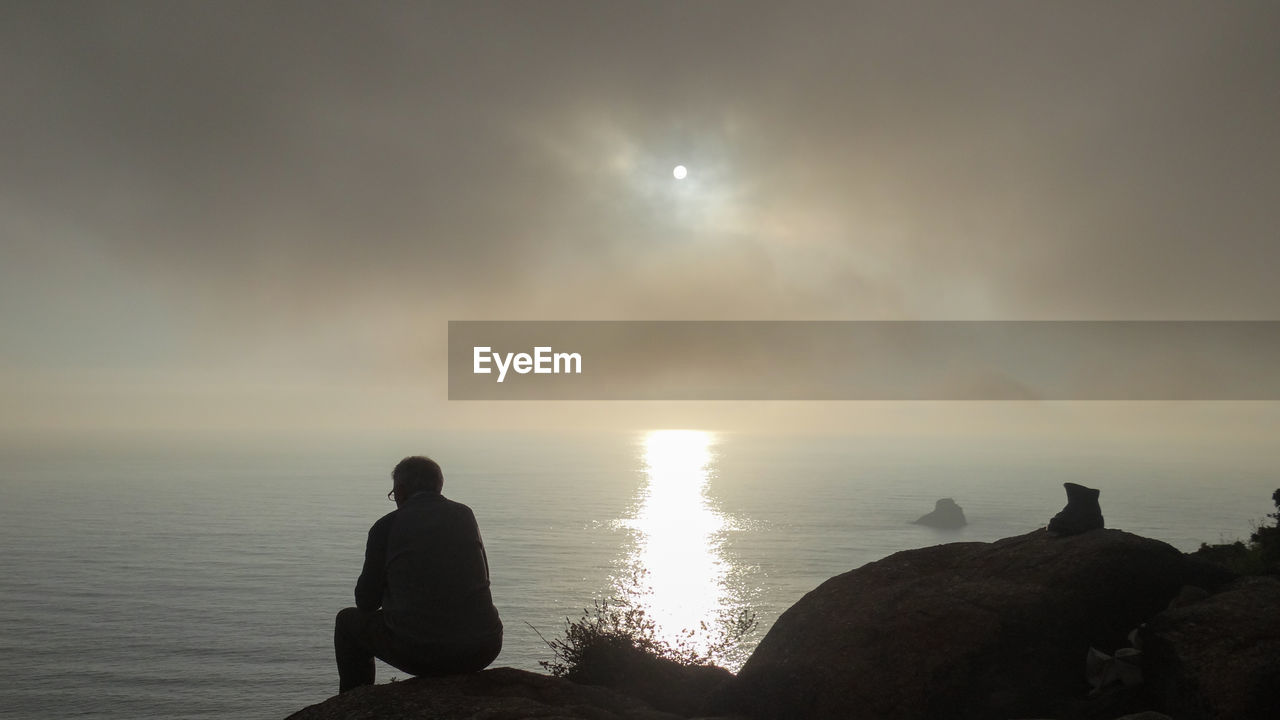 Man sitting on rock at beach against sky