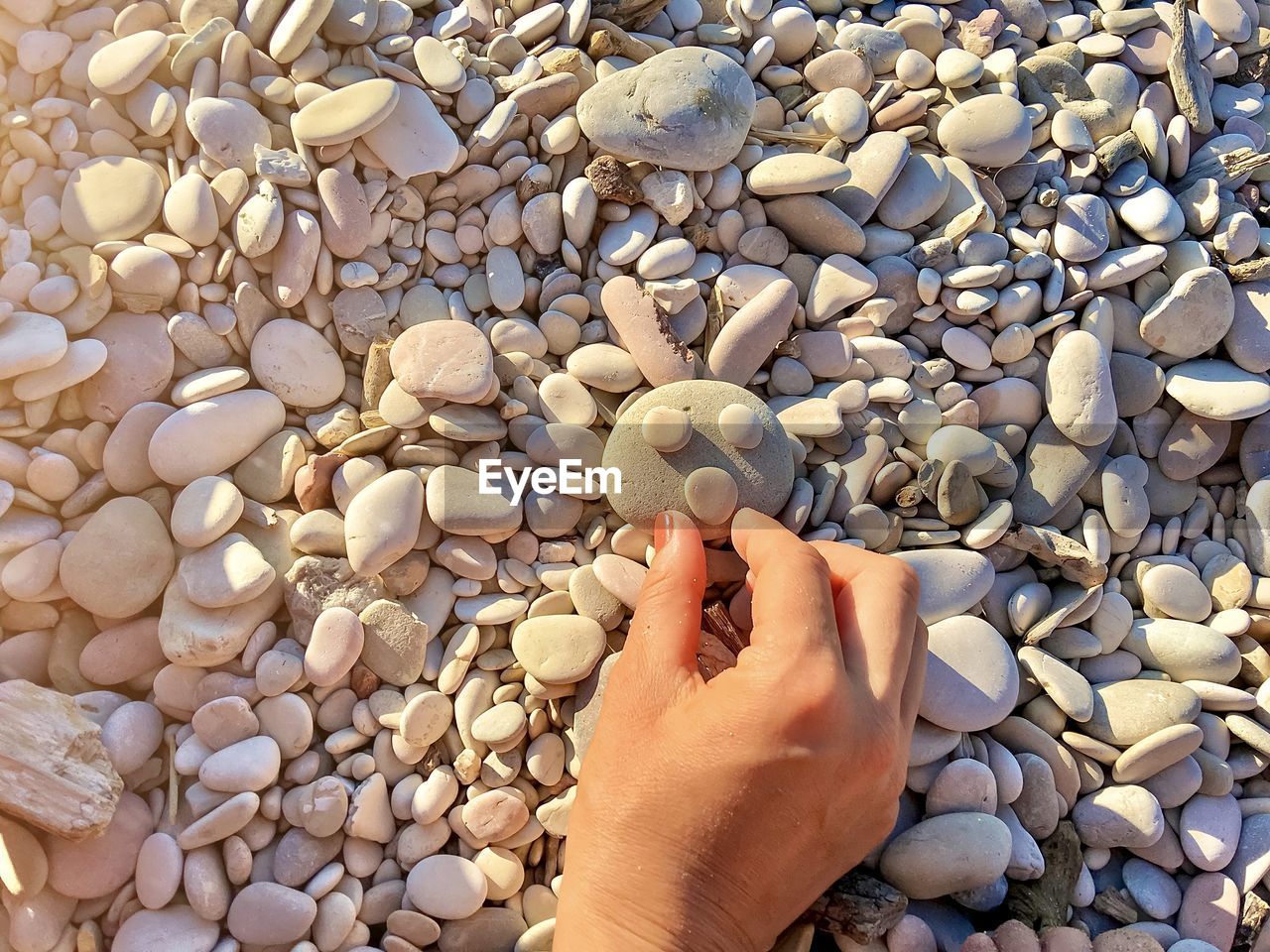 Cropped hand of person arranging stones in a rabbit shape on a stony beach