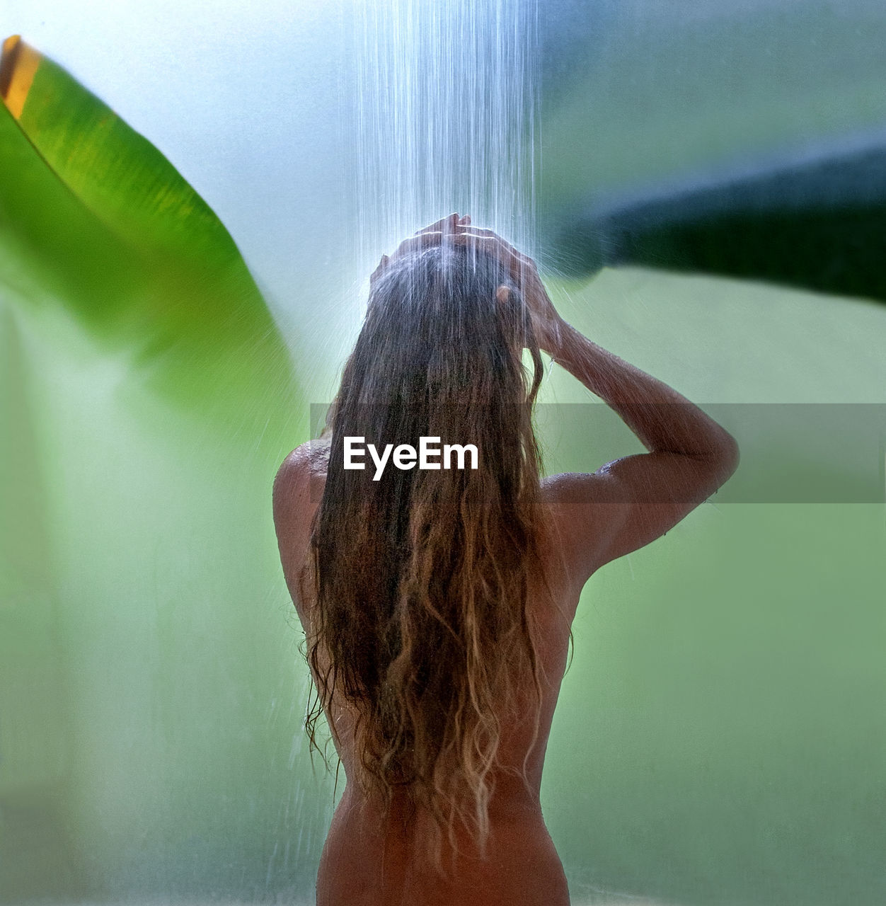 Rear view of shirtless woman bathing under shower