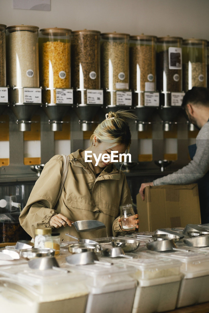 Young woman filling food in container while shopping sustainable store