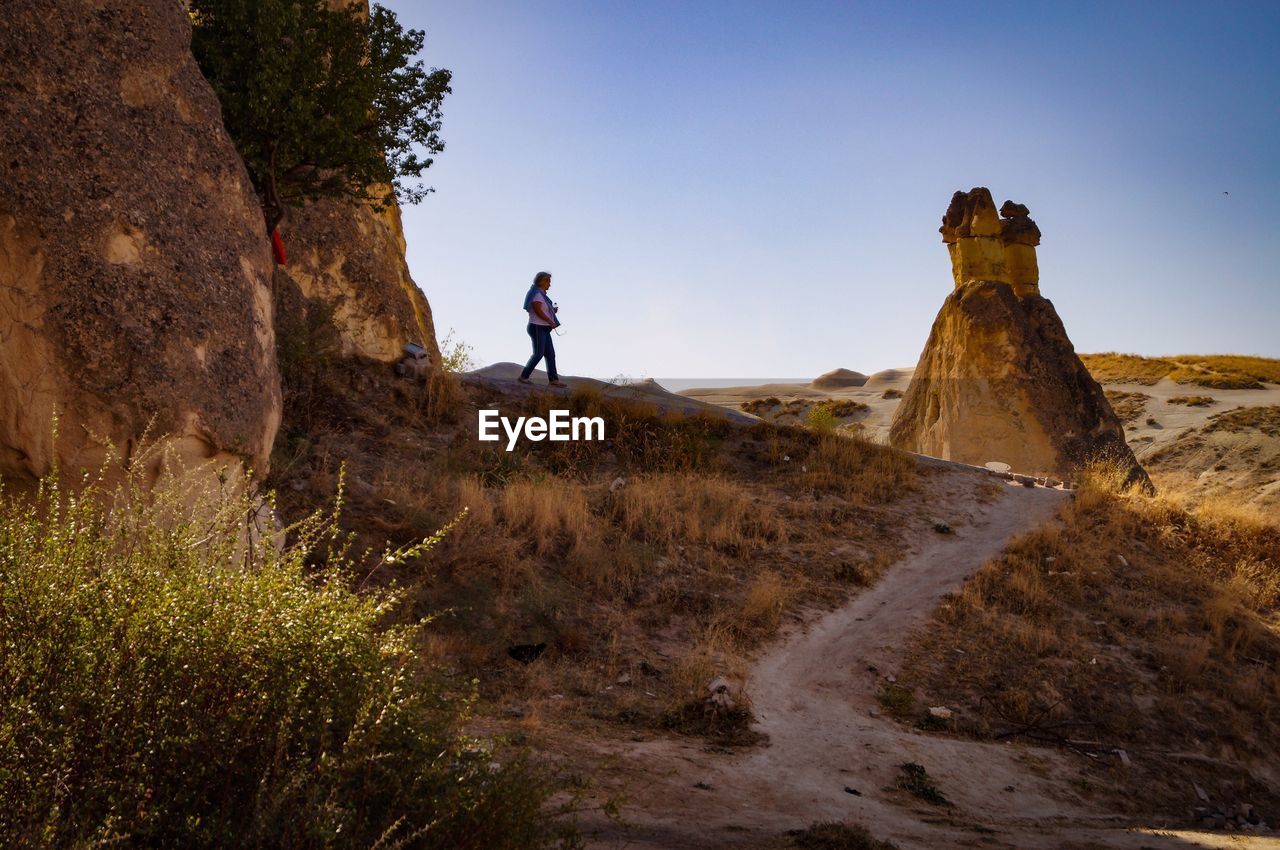 Man standing on rock by land against sky