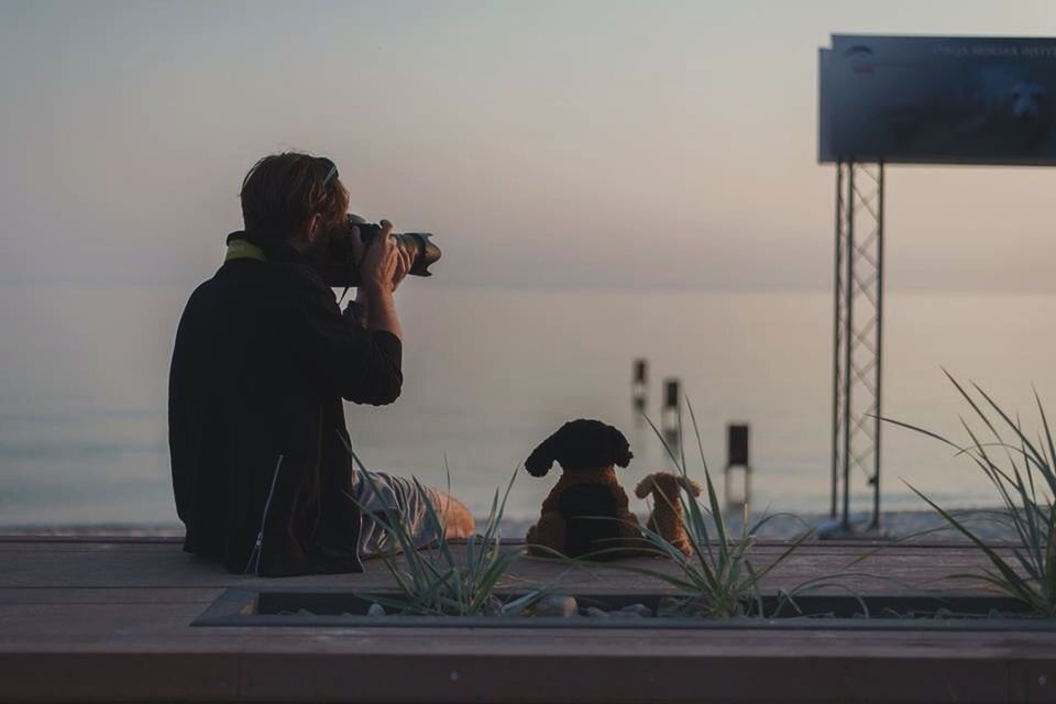 REAR VIEW OF TWO PEOPLE SITTING AT SUNSET