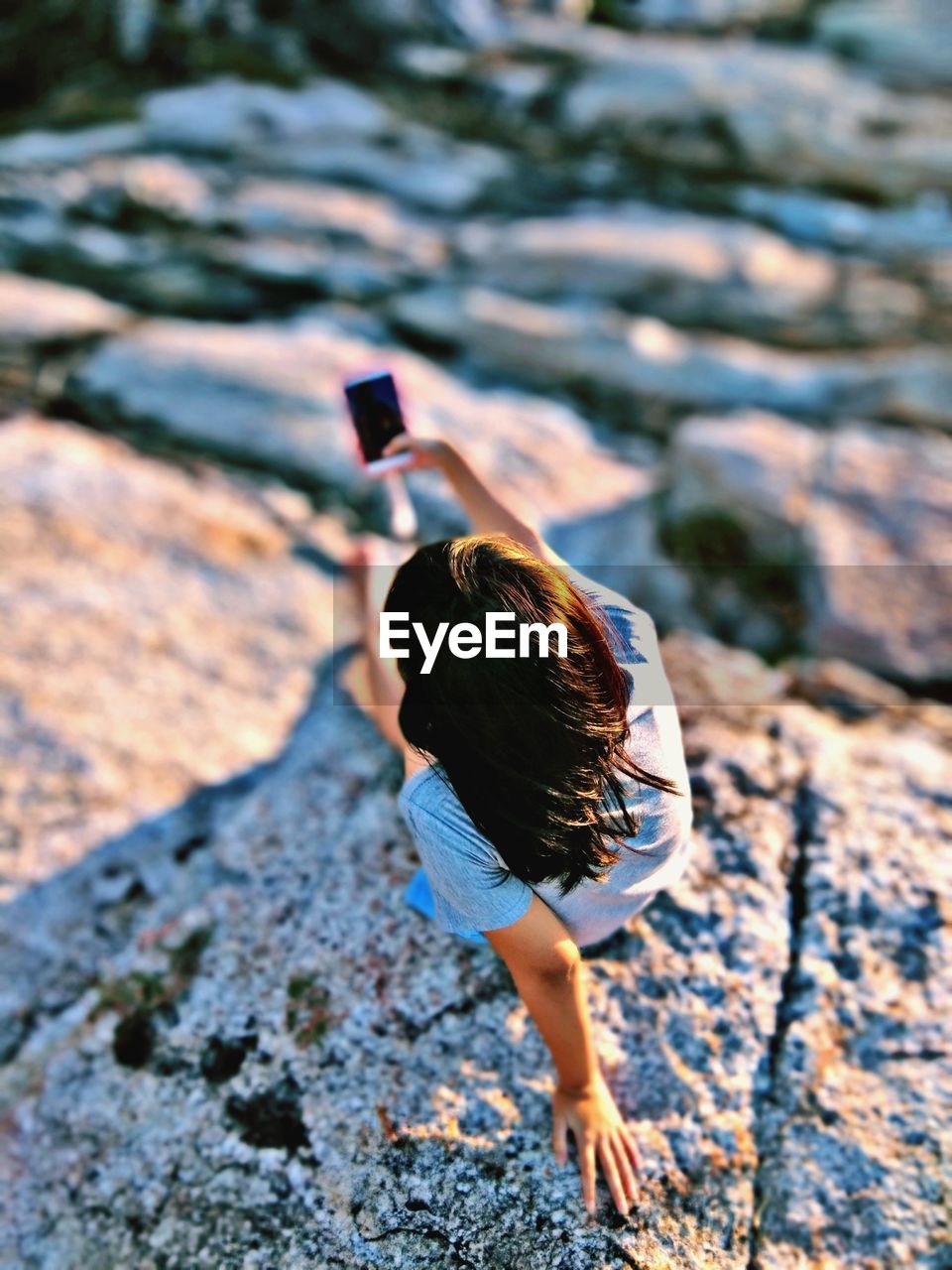 High angle view of woman doing selfie while sitting on rock