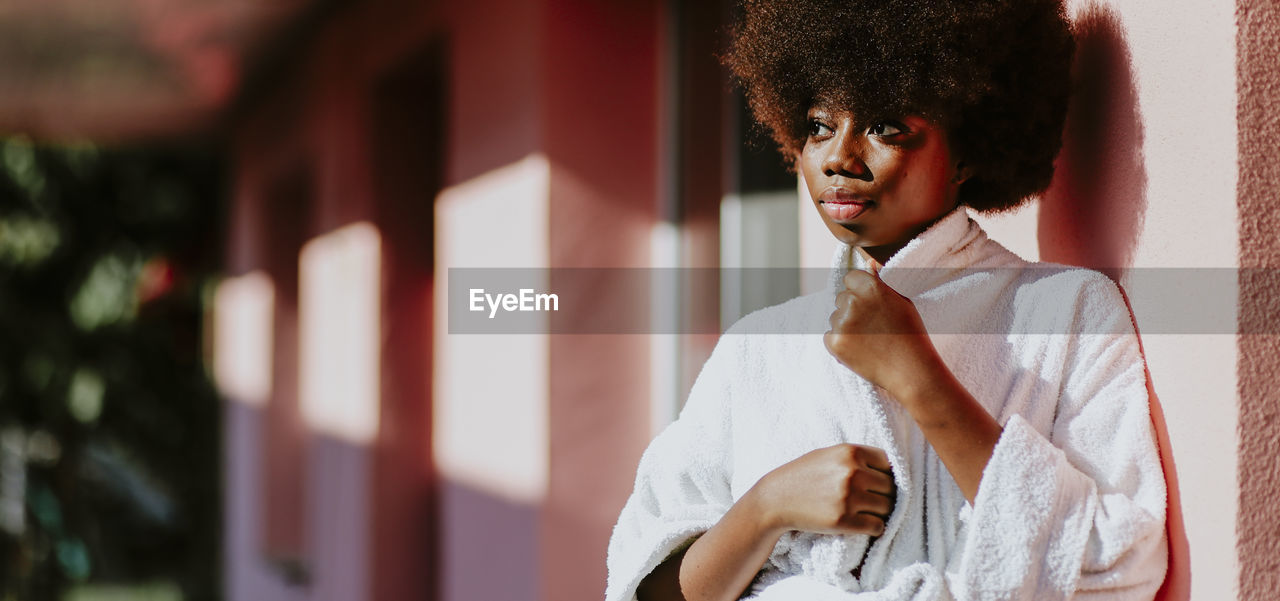 Thoughtful woman with curly hair standing against wall