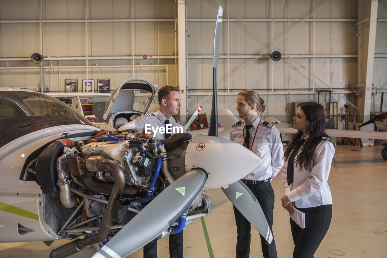 Engineer showing airplane parts to trainees while standing in hangar