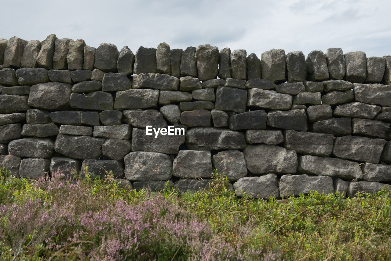 Many various sizes of stones or bricks make up this dry stone wall. peak district heather and plants