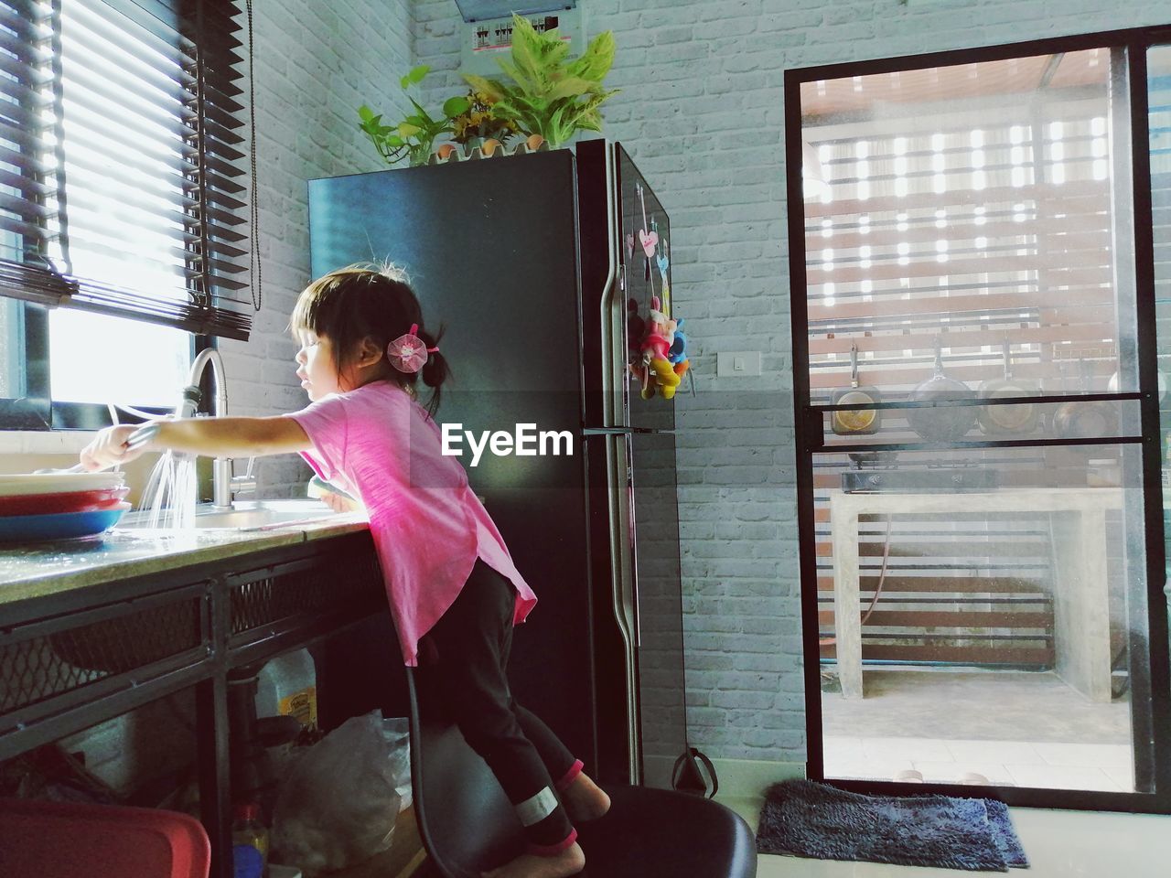 Side view of girl standing by sink and window in kitchen