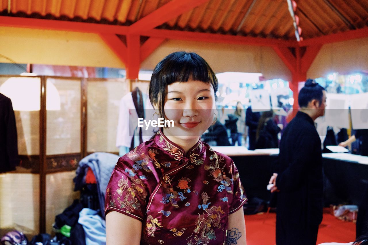 PORTRAIT OF SMILING YOUNG WOMEN STANDING IN CORRIDOR