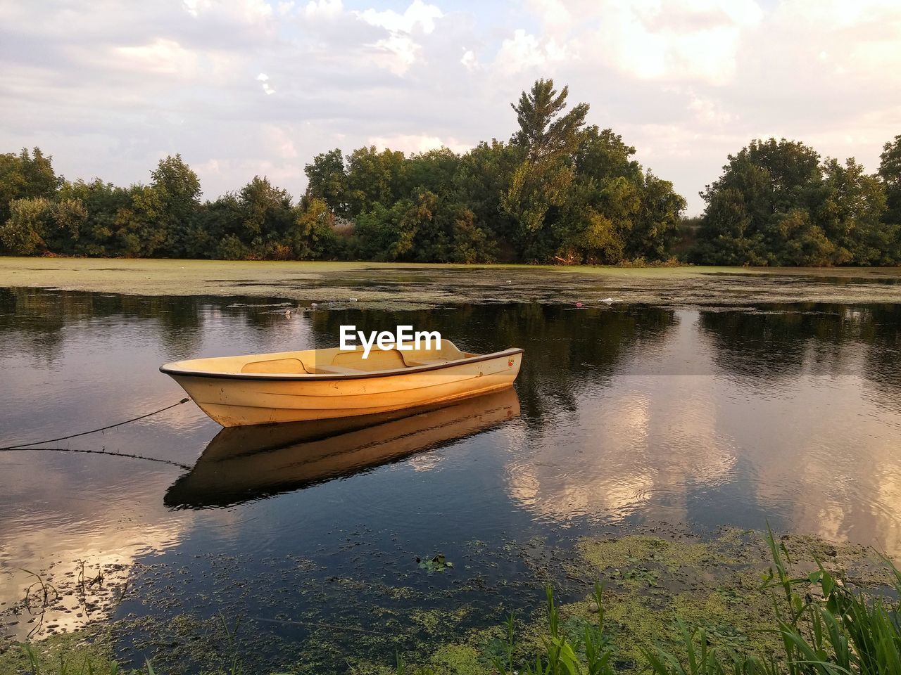 Boat moored on lake by trees against sky