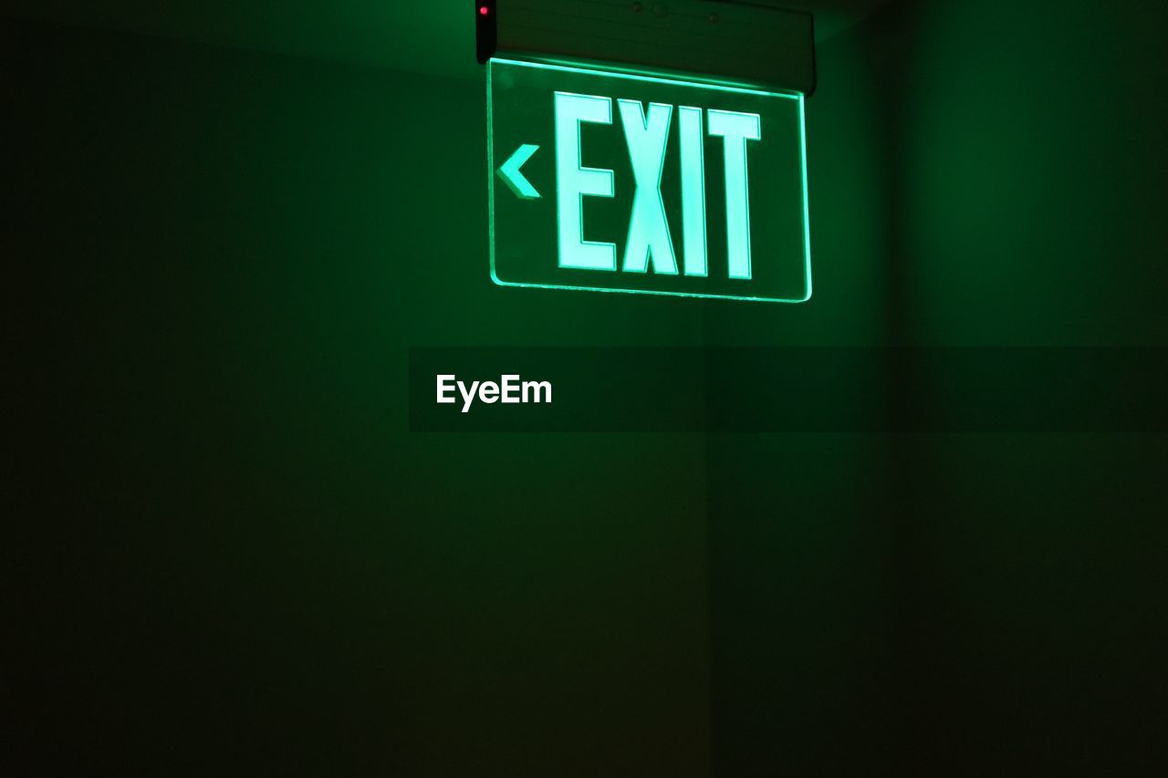 Close-up of illuminated exit sign against wall