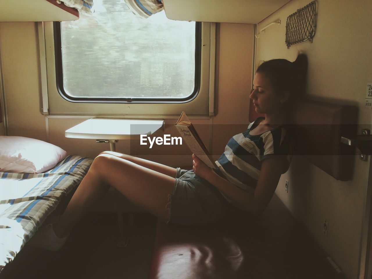Young woman reading book while resting in train