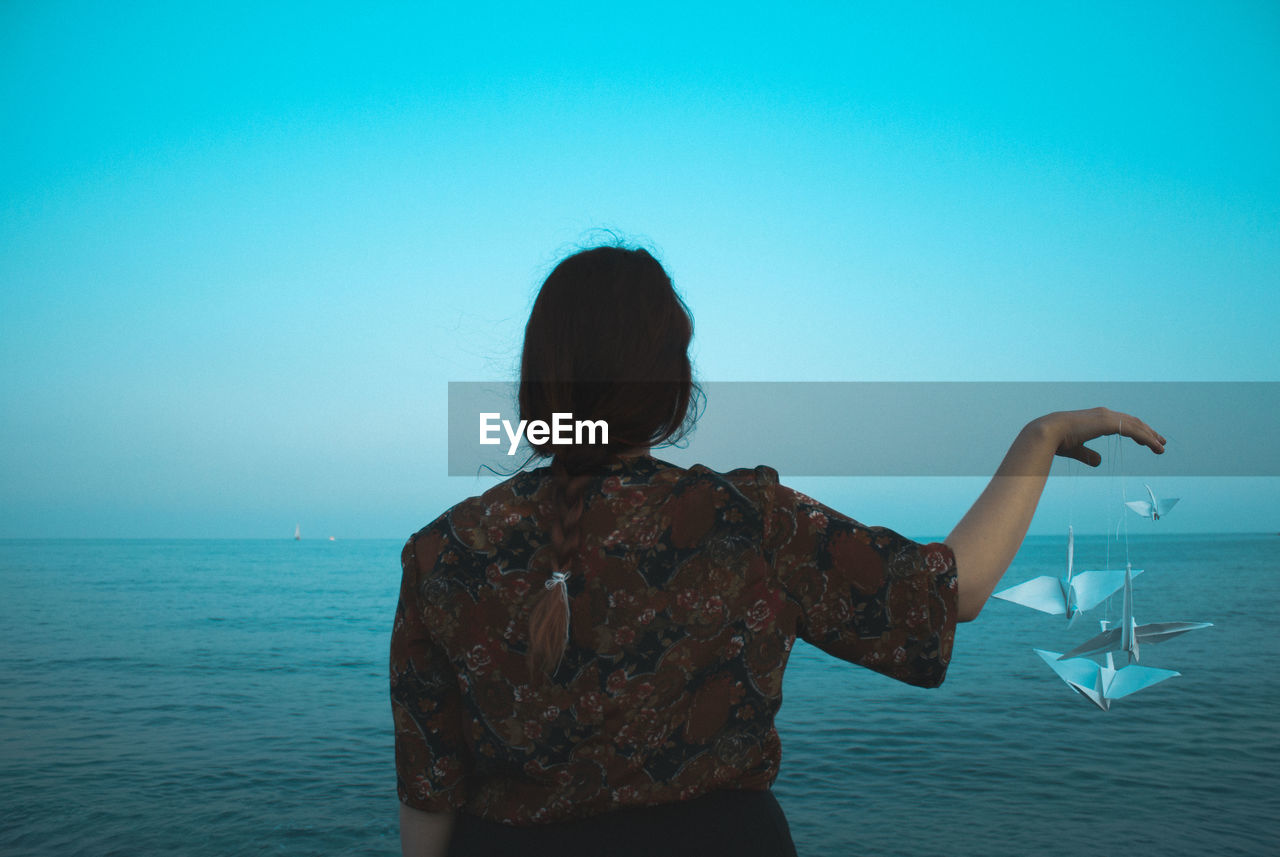 REAR VIEW OF WOMAN BY SEA AGAINST CLEAR SKY